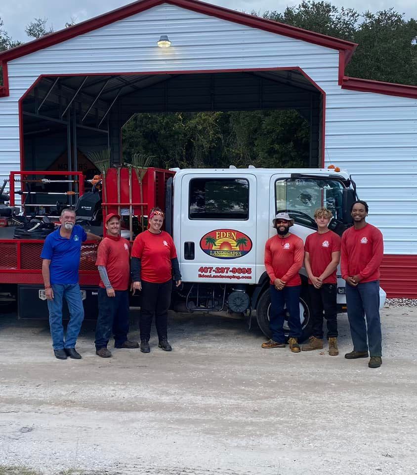 Group of people in red shirts and one in blue posing by a white truck with a logo, in front of a building.