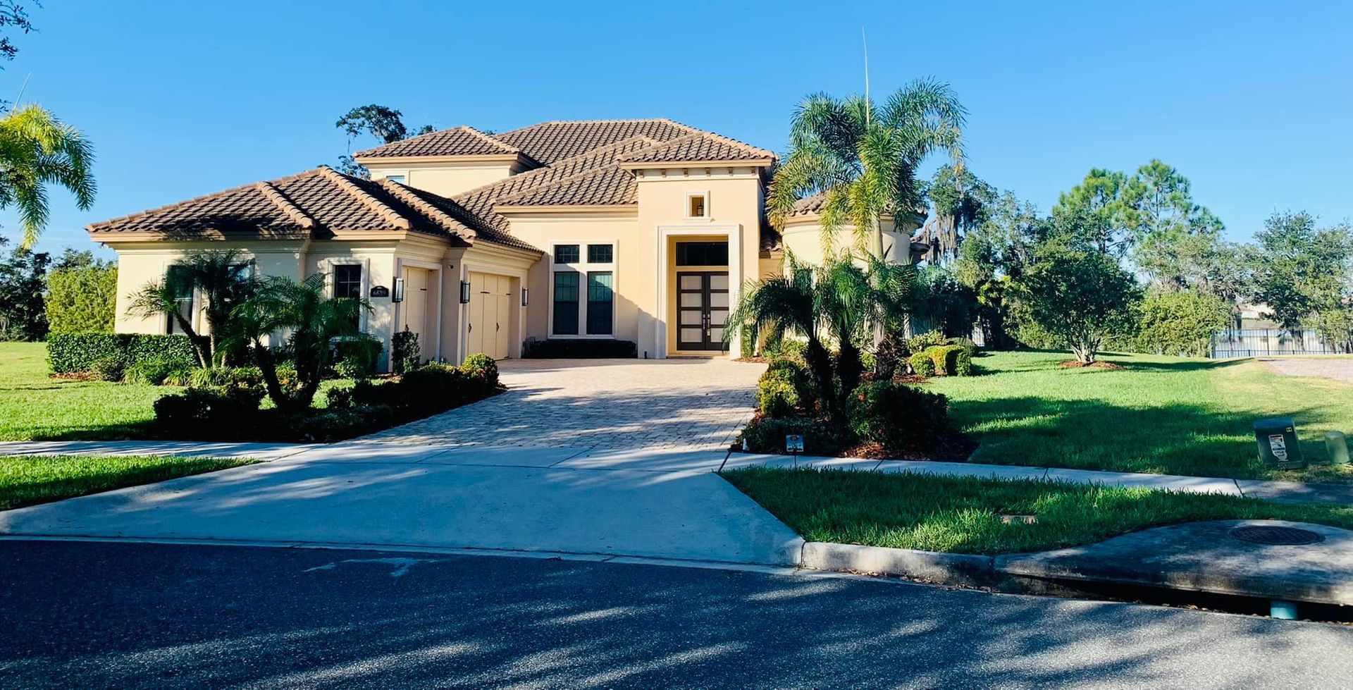 Tan stucco house with clay tile roof, driveway, and palm trees in front yard.