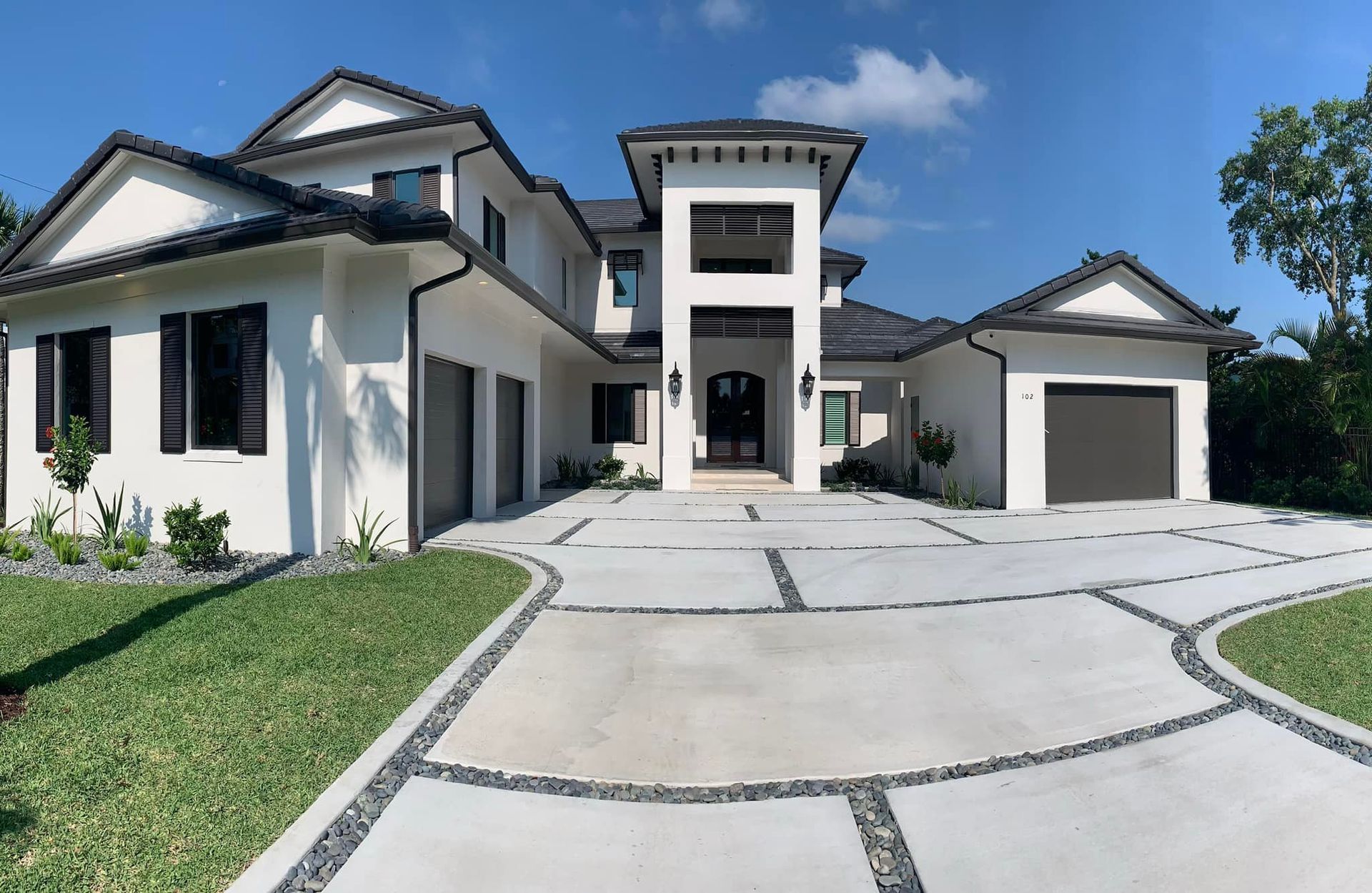 White stucco home with black roof, garage, and driveway on a sunny day.