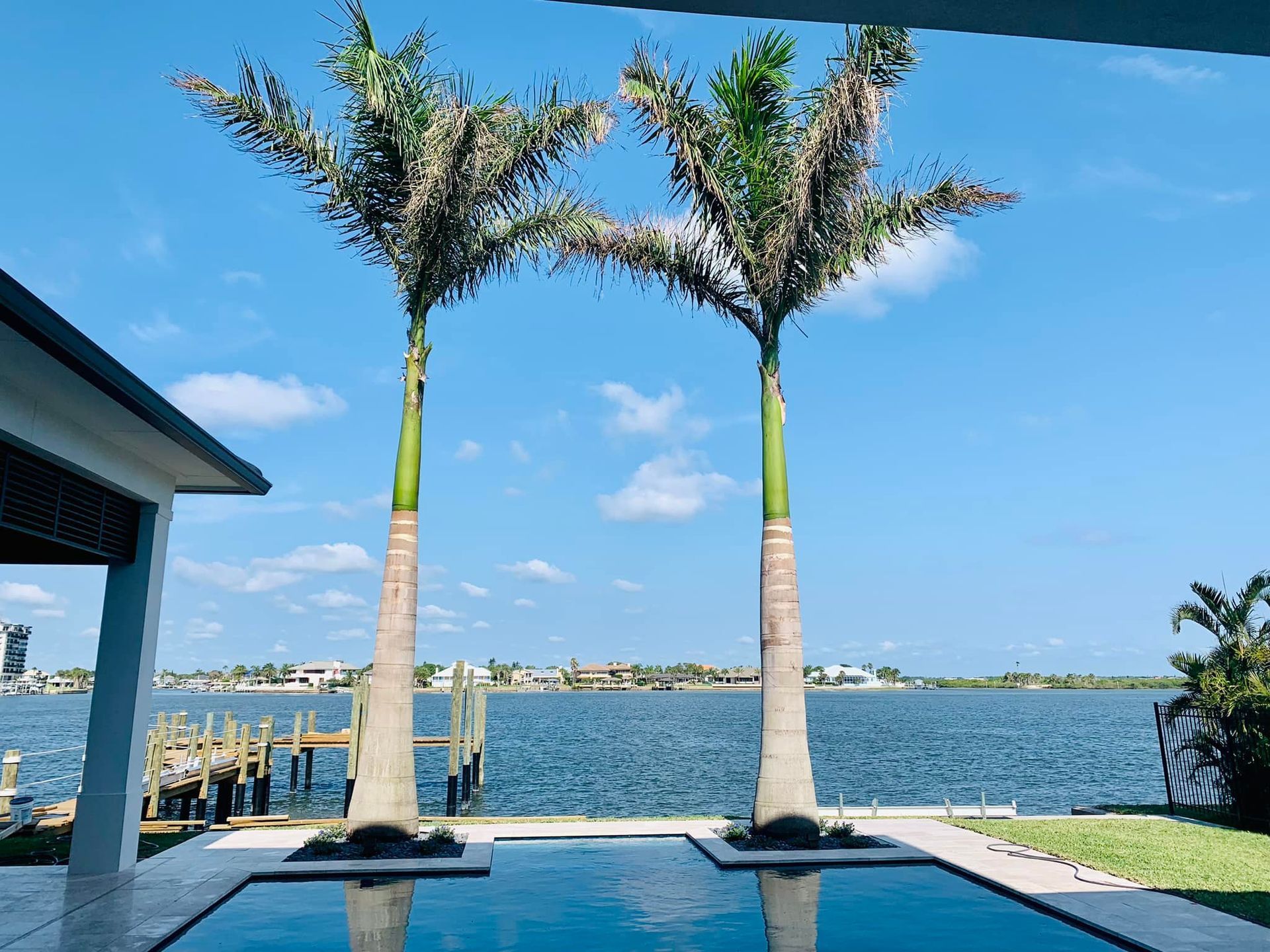 Two palm trees frame a pool overlooking a waterway on a sunny day.