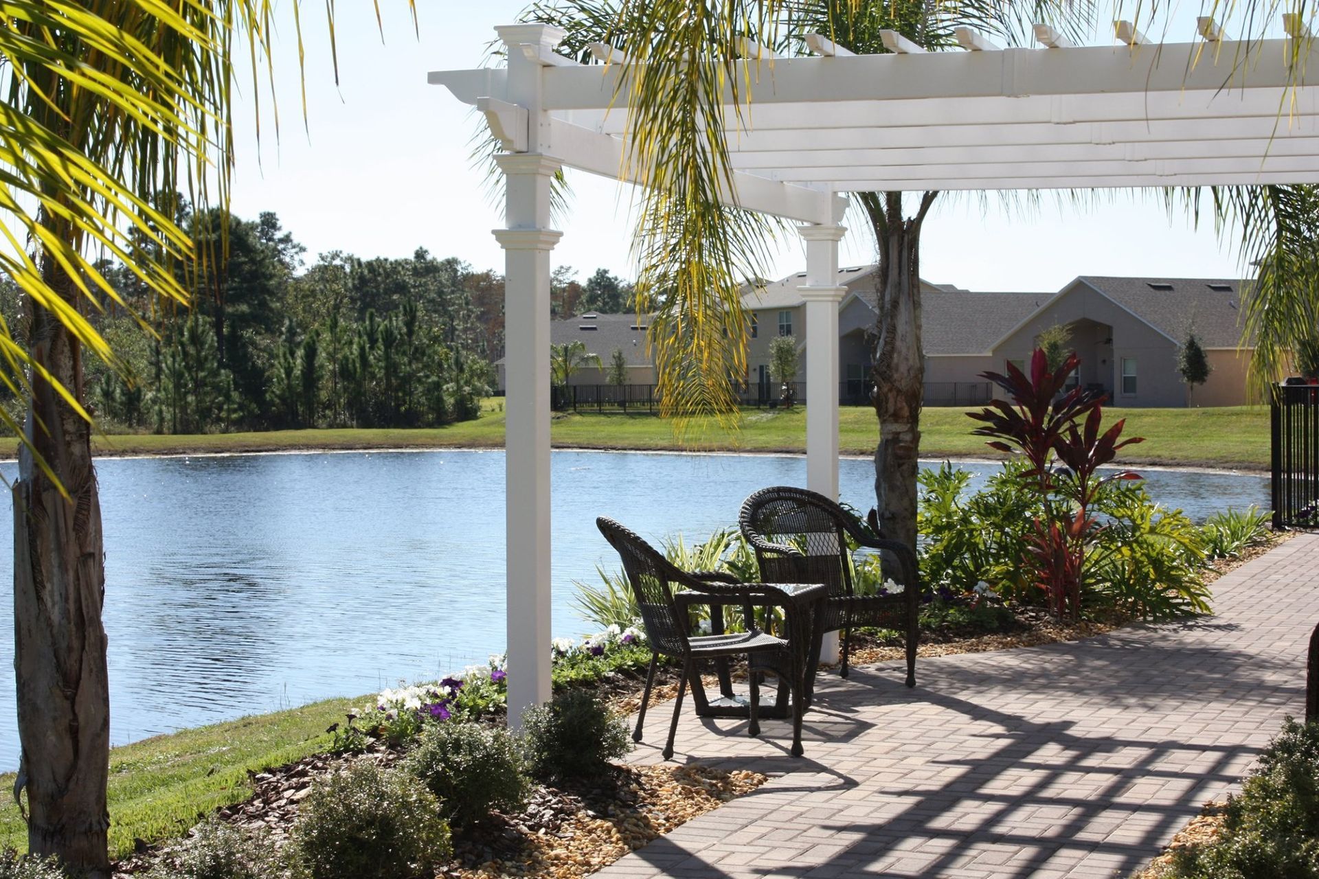 Patio with table and chairs under a white pergola, overlooking a lake.