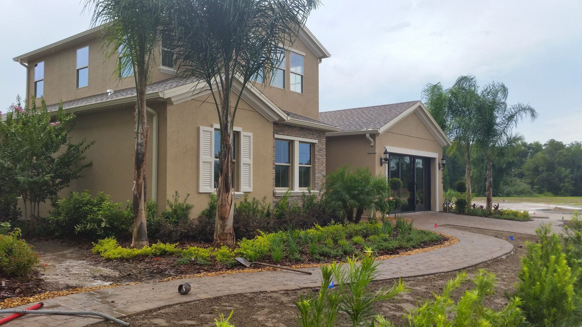 Two-story beige house with stone accents, landscaped yard, and curved walkway.