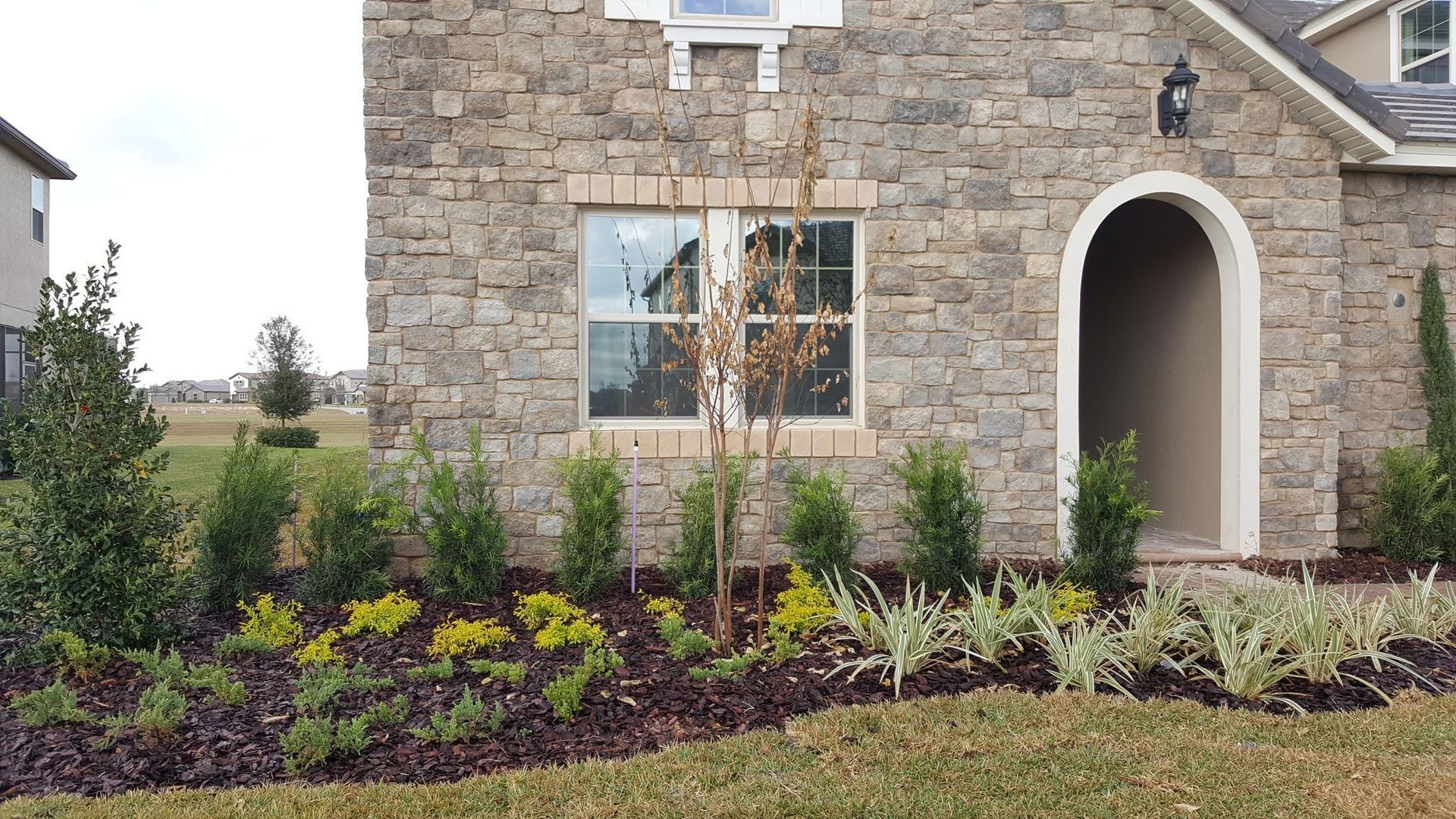 Stone facade home with a window, arched entry, and landscaped front yard.