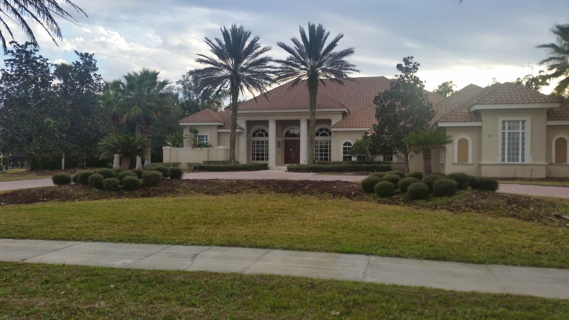 Large beige house with palm trees in front, set in a green lawn.