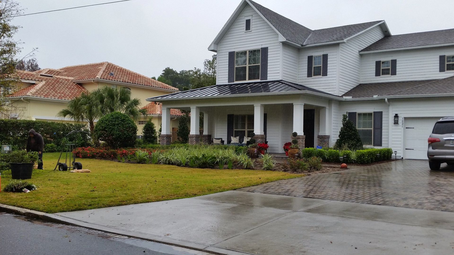 White two-story house with black shutters, covered porch, and landscaped yard. A car is parked in the driveway.