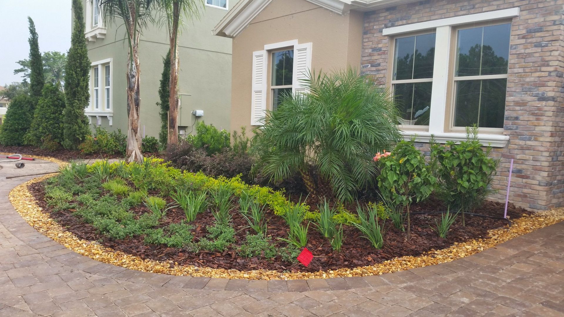 Landscaped yard with colorful plants, mulch, and stone edging in front of a house.