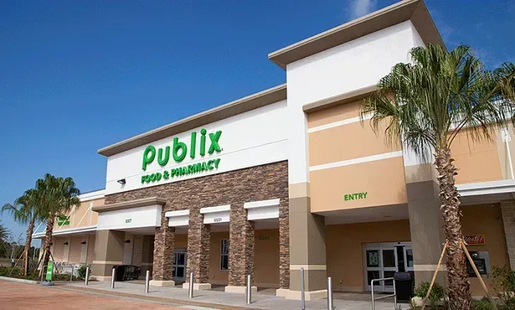 Publix grocery store exterior with green sign, palm trees, and clear blue sky.