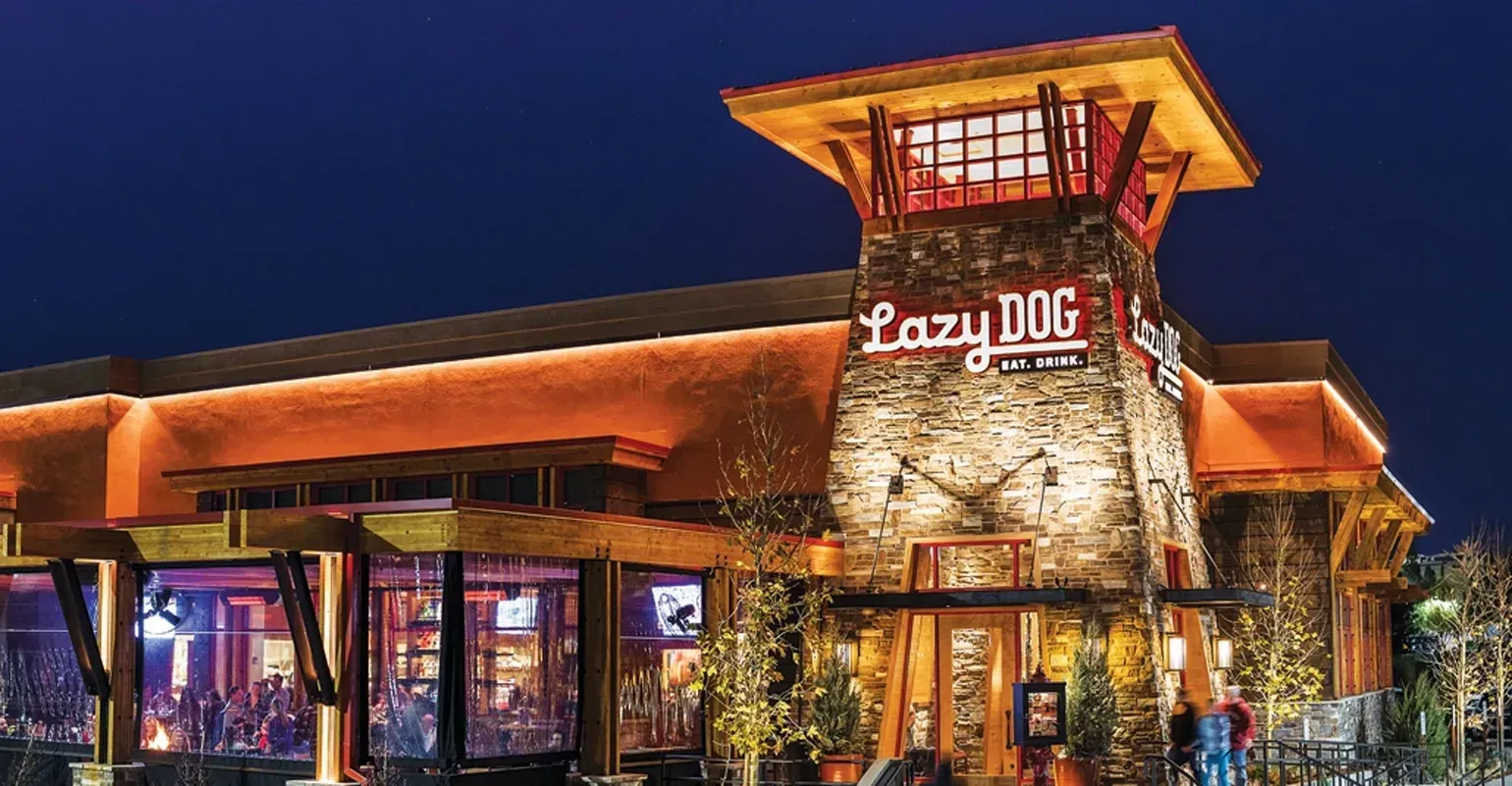 Lazy Dog Restaurant exterior at night, with stone tower and orange lighting.