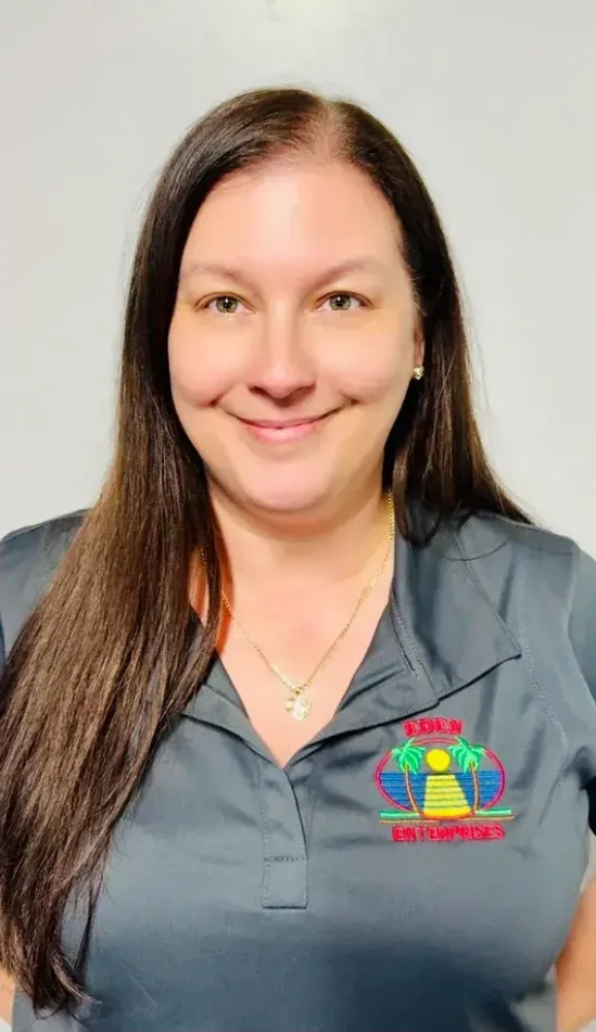 Woman with long brown hair wearing a gray polo shirt, smiling, in front of a white background.