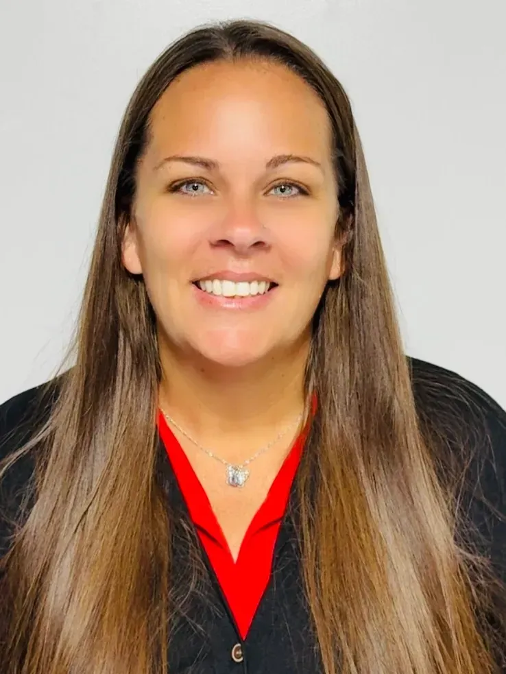 Woman with long brown hair smiles, wearing a red shirt under a black jacket.