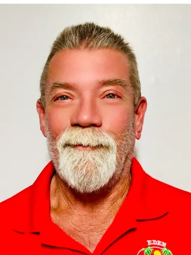Man with graying hair and beard wearing a red shirt, smiling.