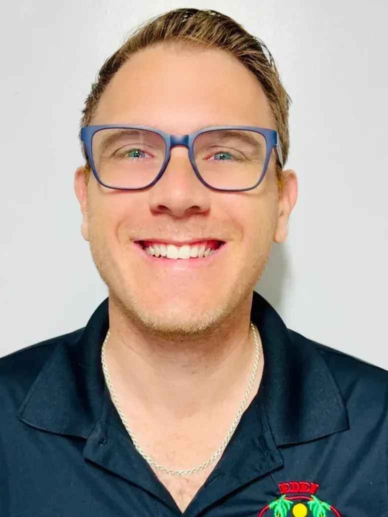 Man with glasses smiling, wearing a dark blue collared shirt.