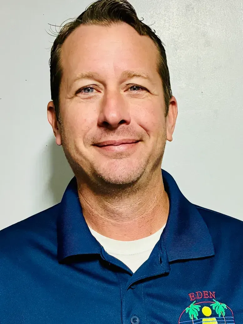 Man in blue polo shirt smiling, with a logo on the shirt.