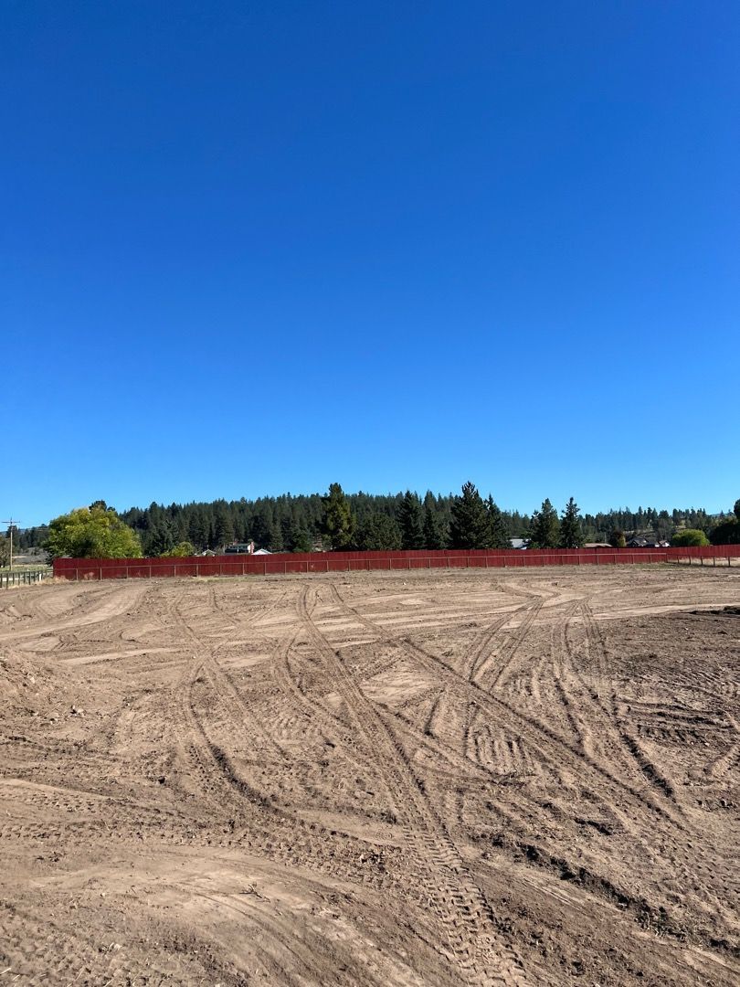 Cleared land with tire tracks, red barrier, trees in the distance under a bright blue sky.