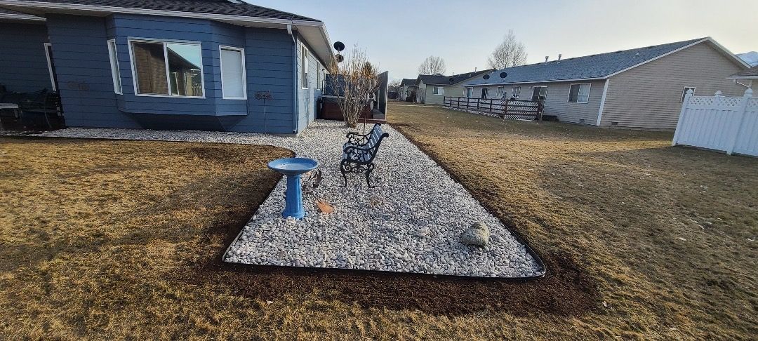 A backyard with a gravel garden bed, bird bath, and a blue house.