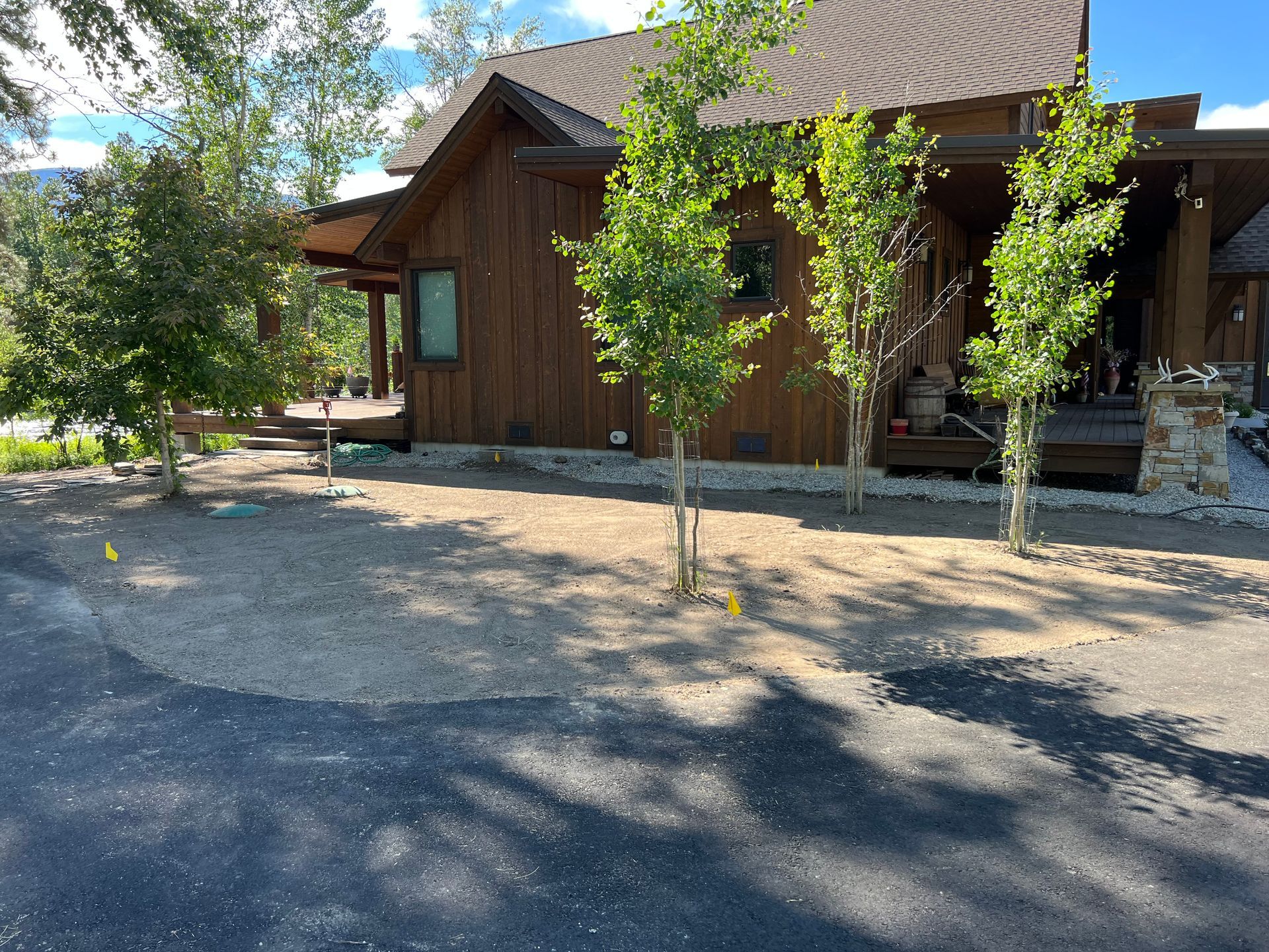 Brown house with trees, gravel, and driveway. Sunny outdoor setting.