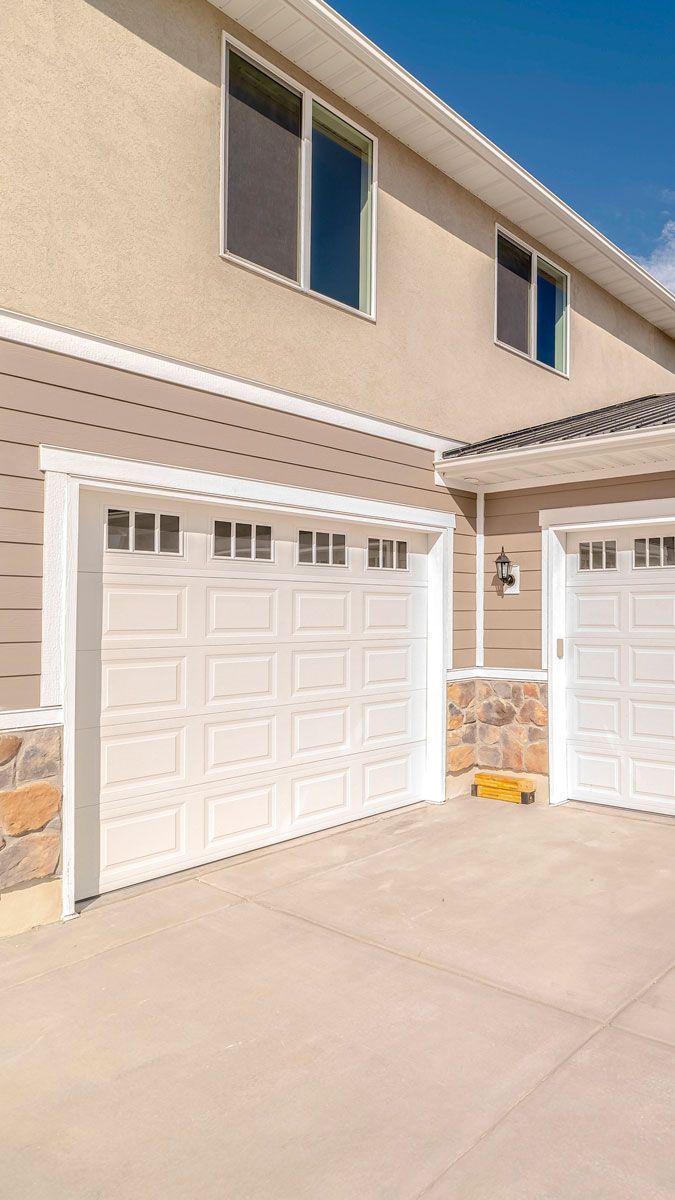 Two-car garage with white doors and tan siding on a house with concrete driveway and stone accents.