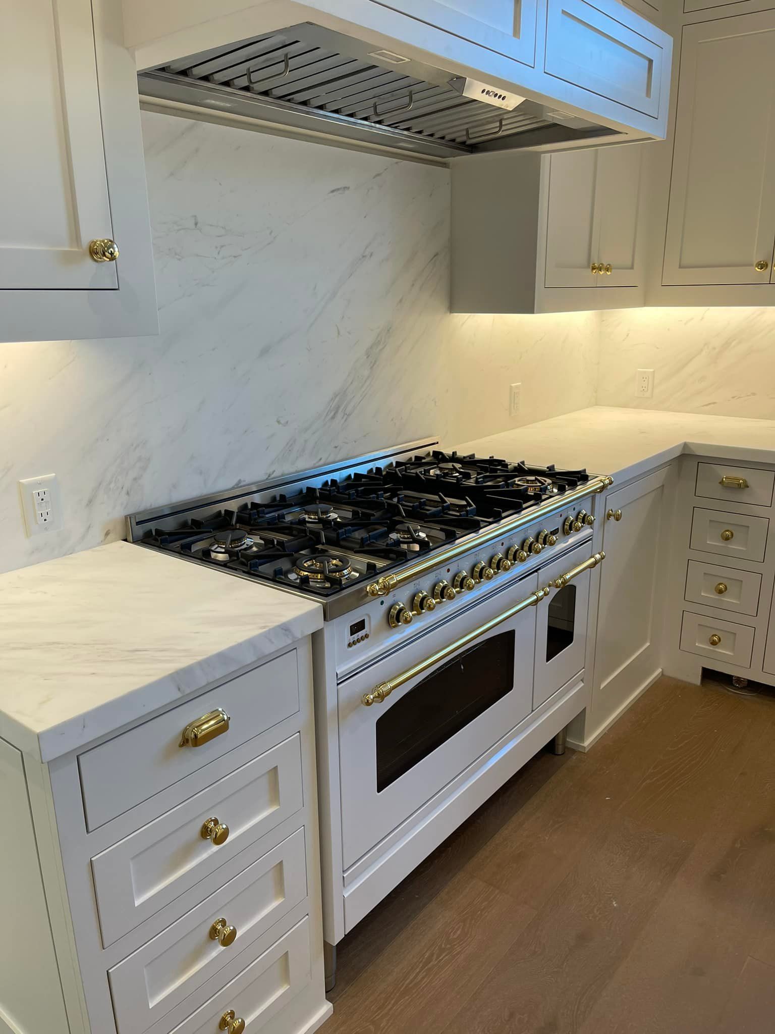 White kitchen with a large gas range, marble countertops, and gold hardware.