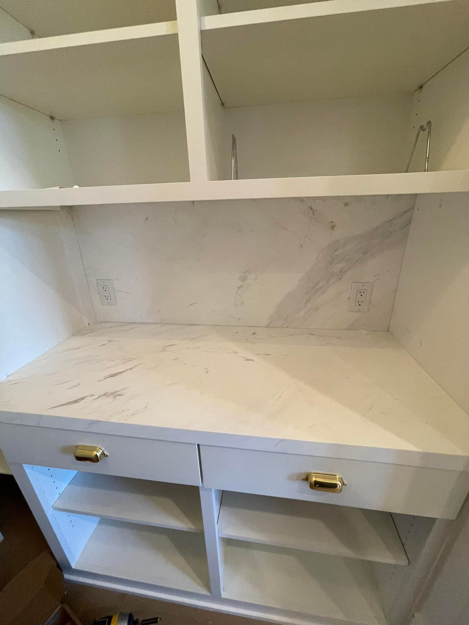 White built-in cabinet with shelves, drawers, and gold handles, likely in a home.
