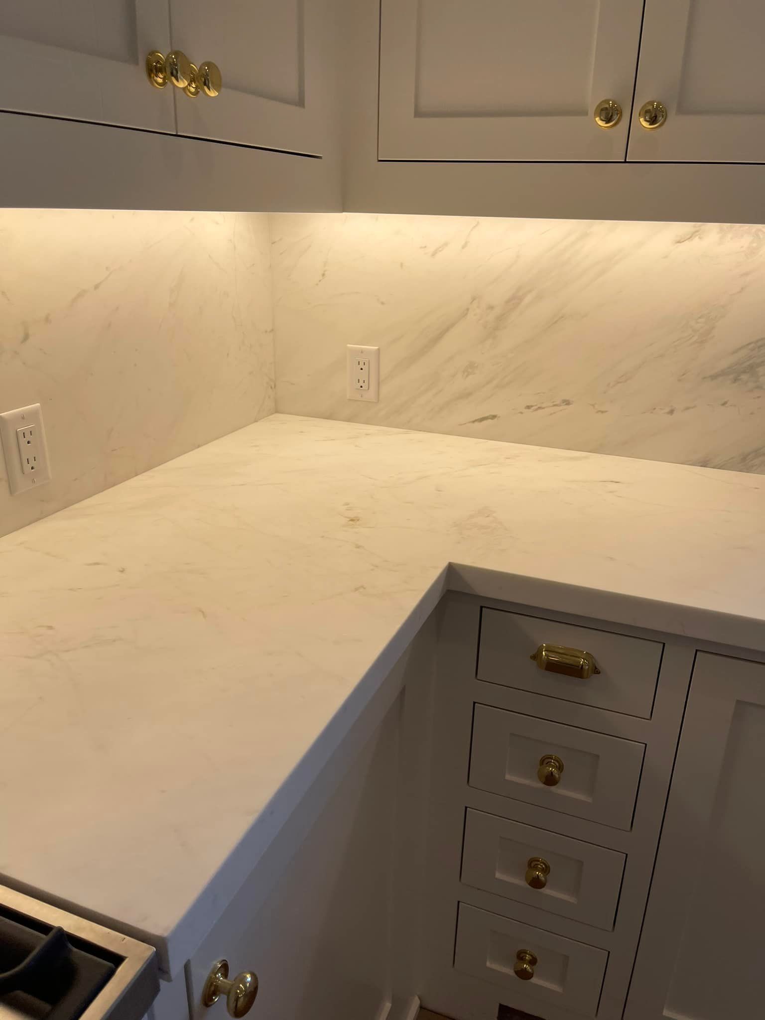 White marble kitchen countertop with a backsplash and white cabinets with gold knobs.