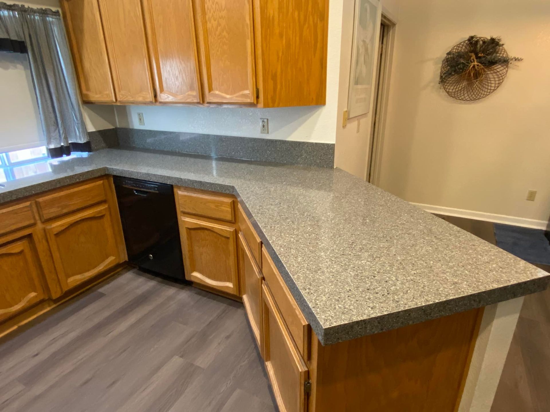 Kitchen with wooden cabinets, gray countertop, black appliances, and gray flooring.