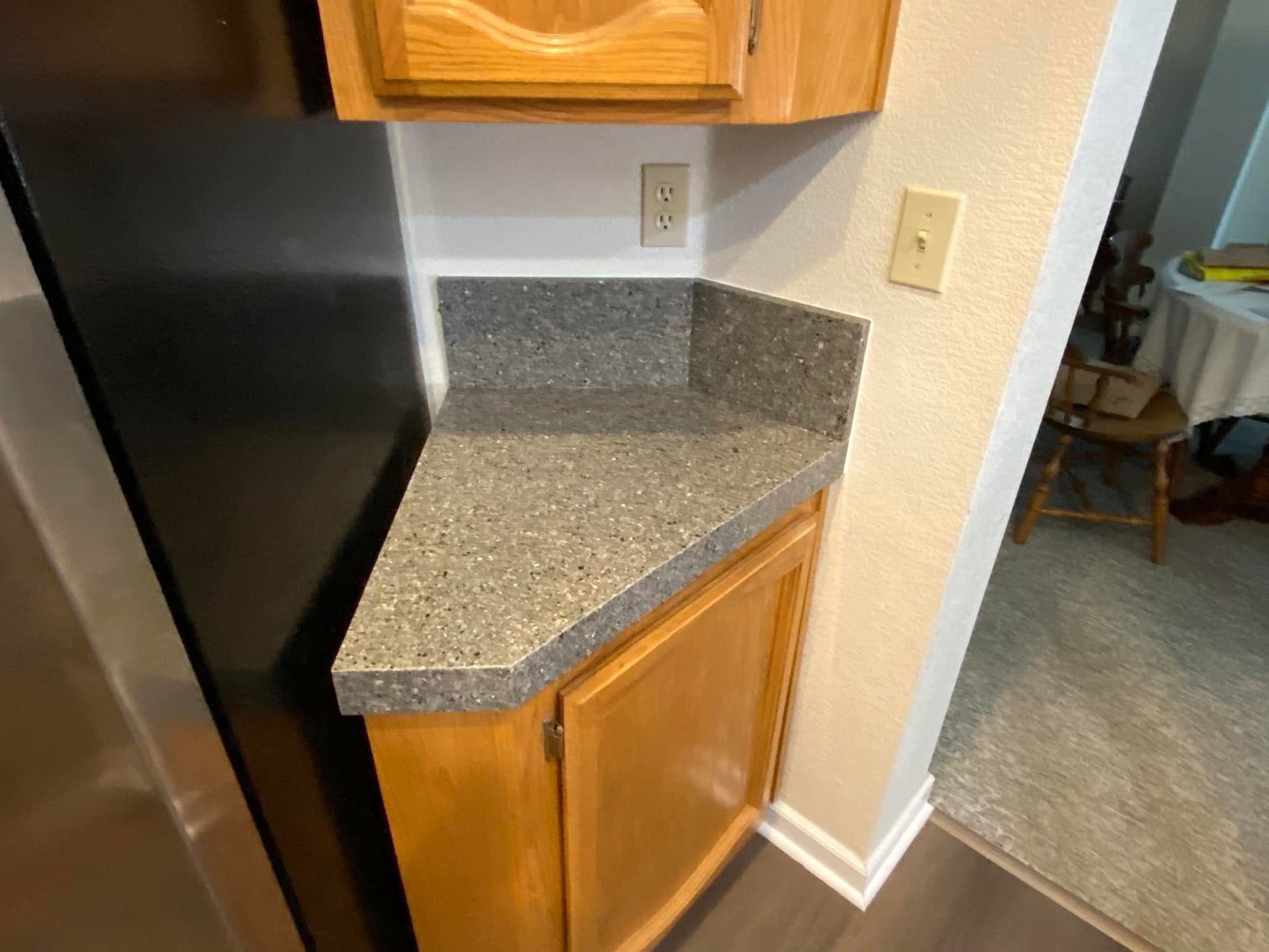 Kitchen corner with a gray countertop, tan cabinets, and a wall outlet.