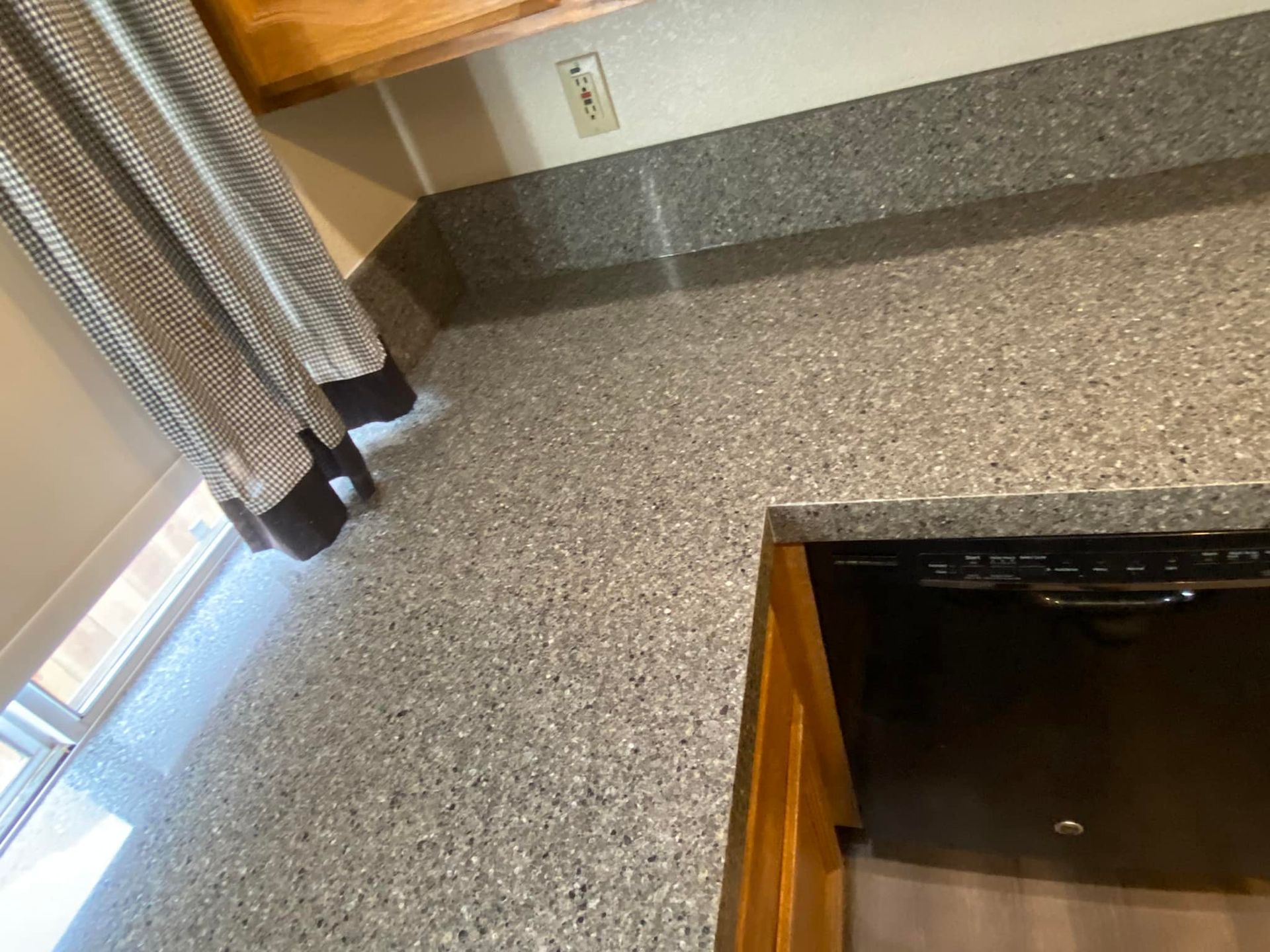 Gray speckled countertop, next to a dishwasher and window with a striped curtain.