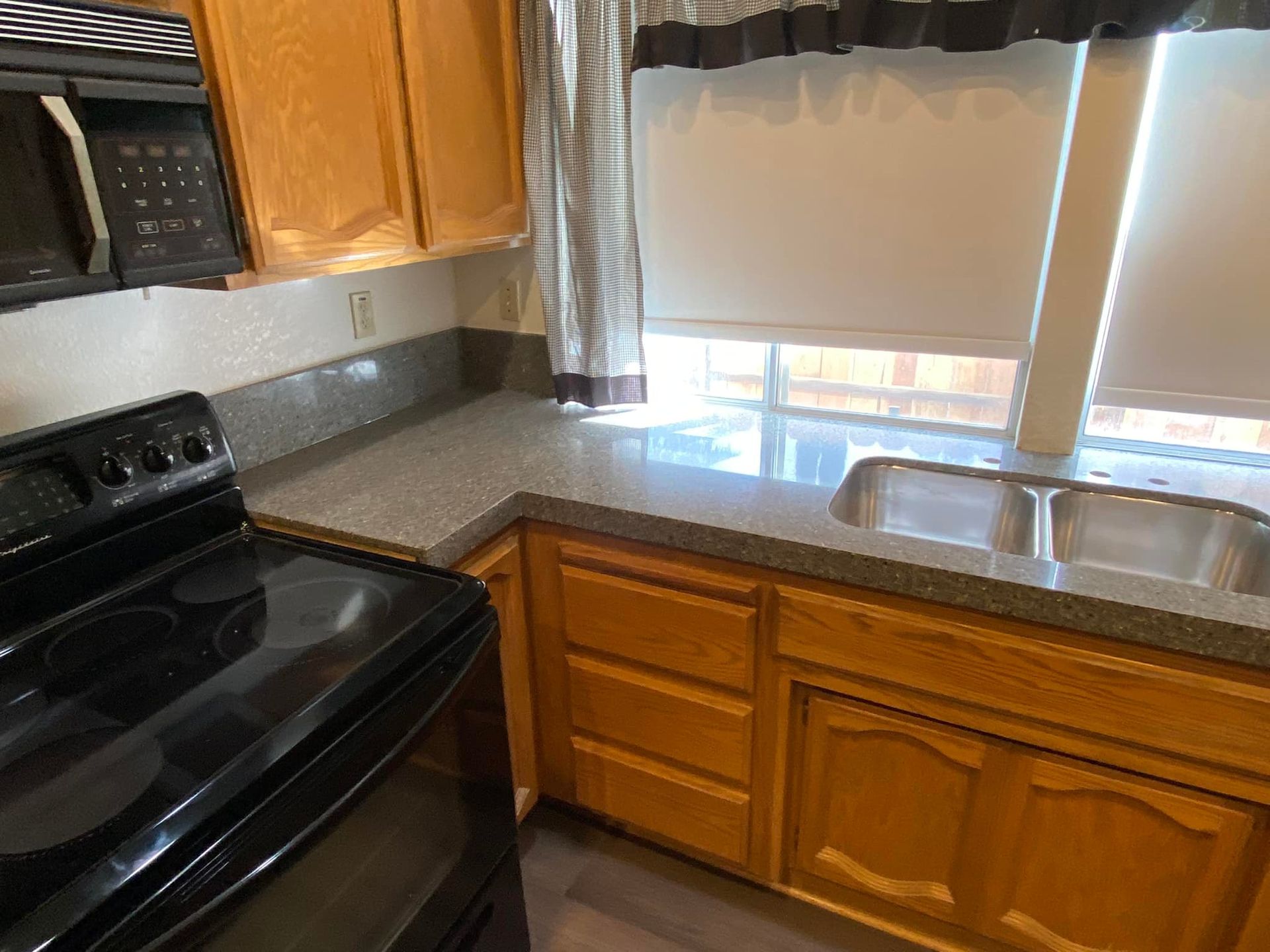 Kitchen with wooden cabinets, grey countertops, and a black stove. A window is above the sink.