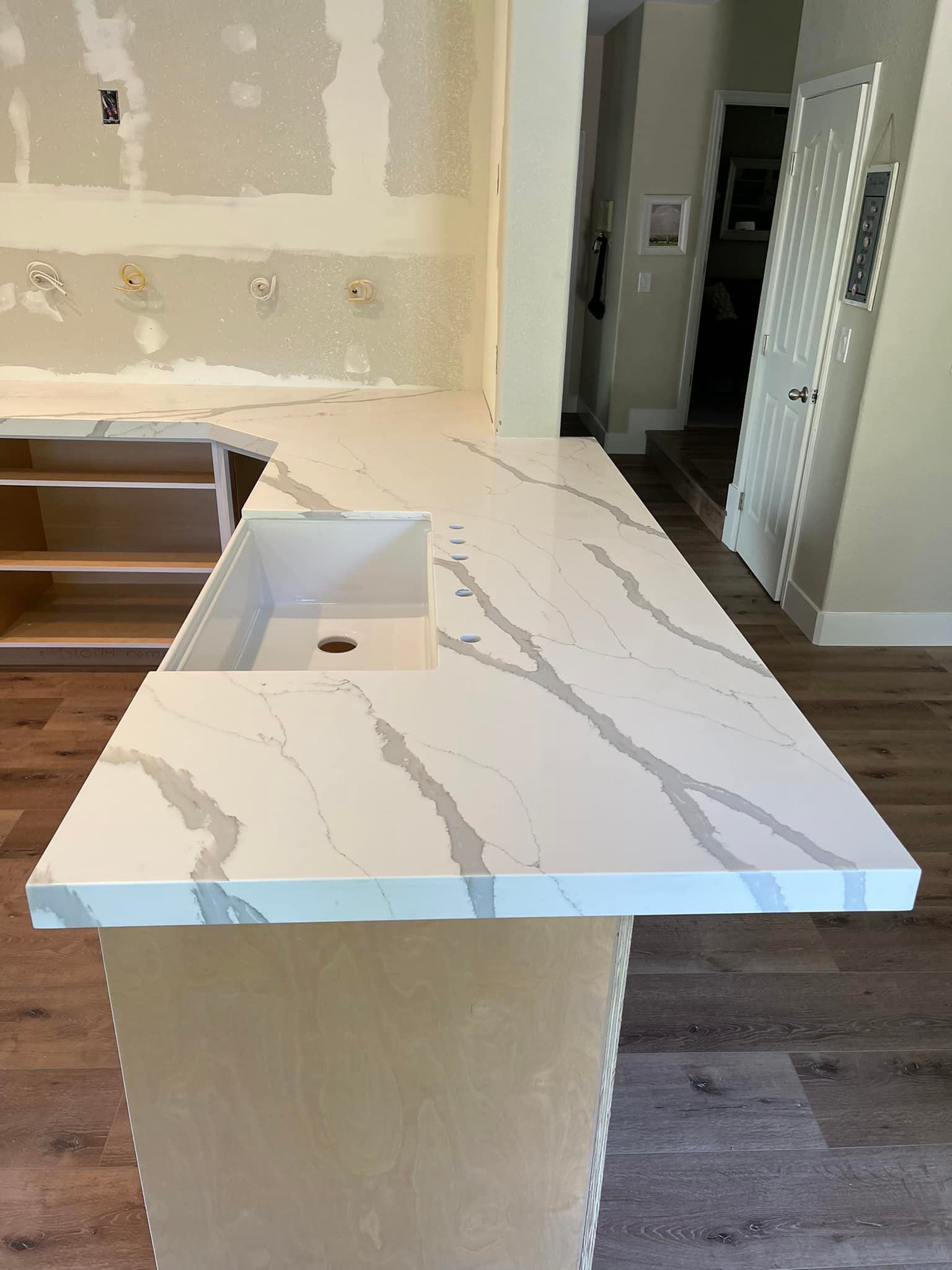 A white quartz countertop with gray veining installed in a kitchen with unfinished cabinets.