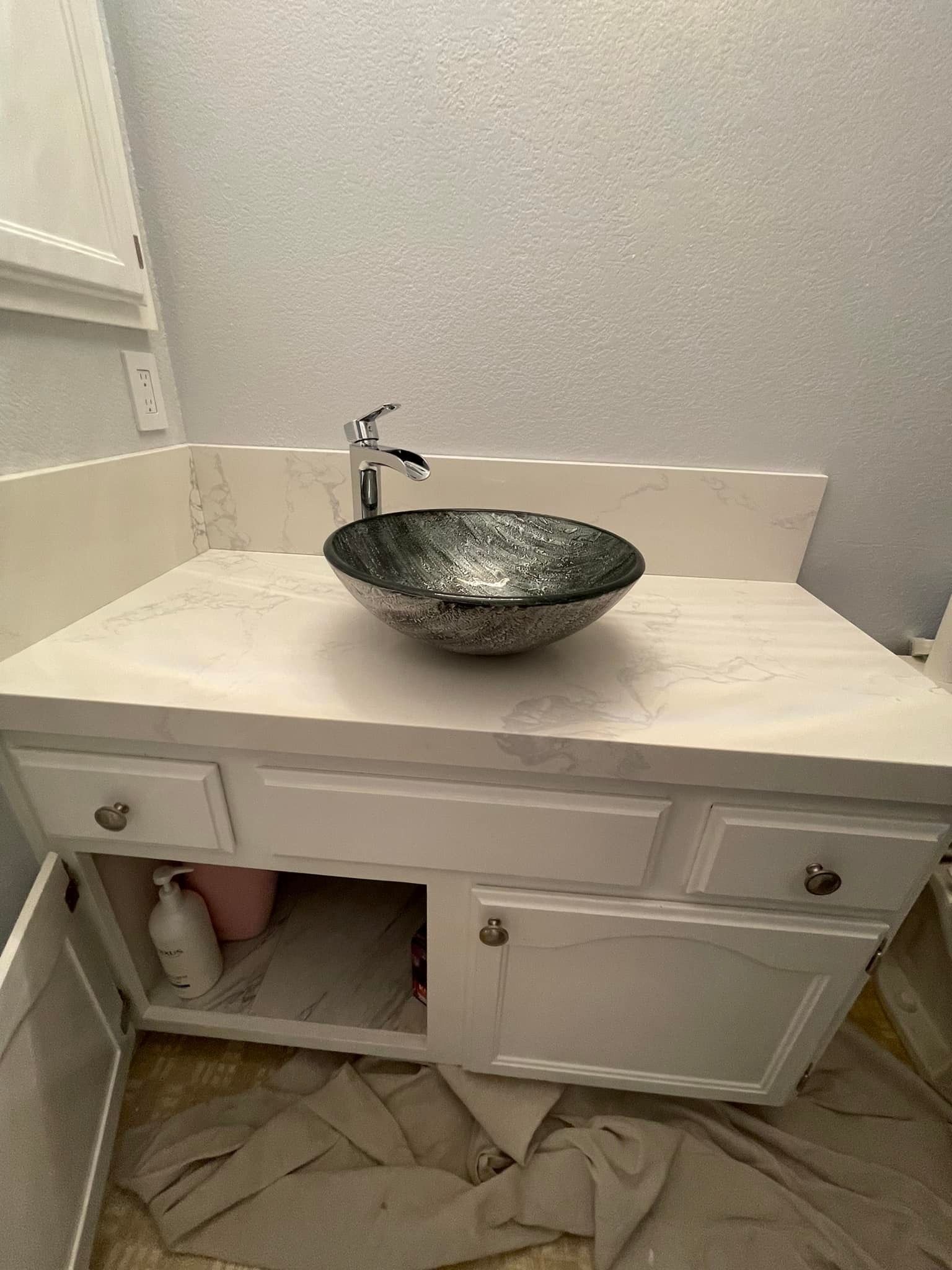 White vanity with a dark glass bowl sink, faucet, and open cabinet doors.