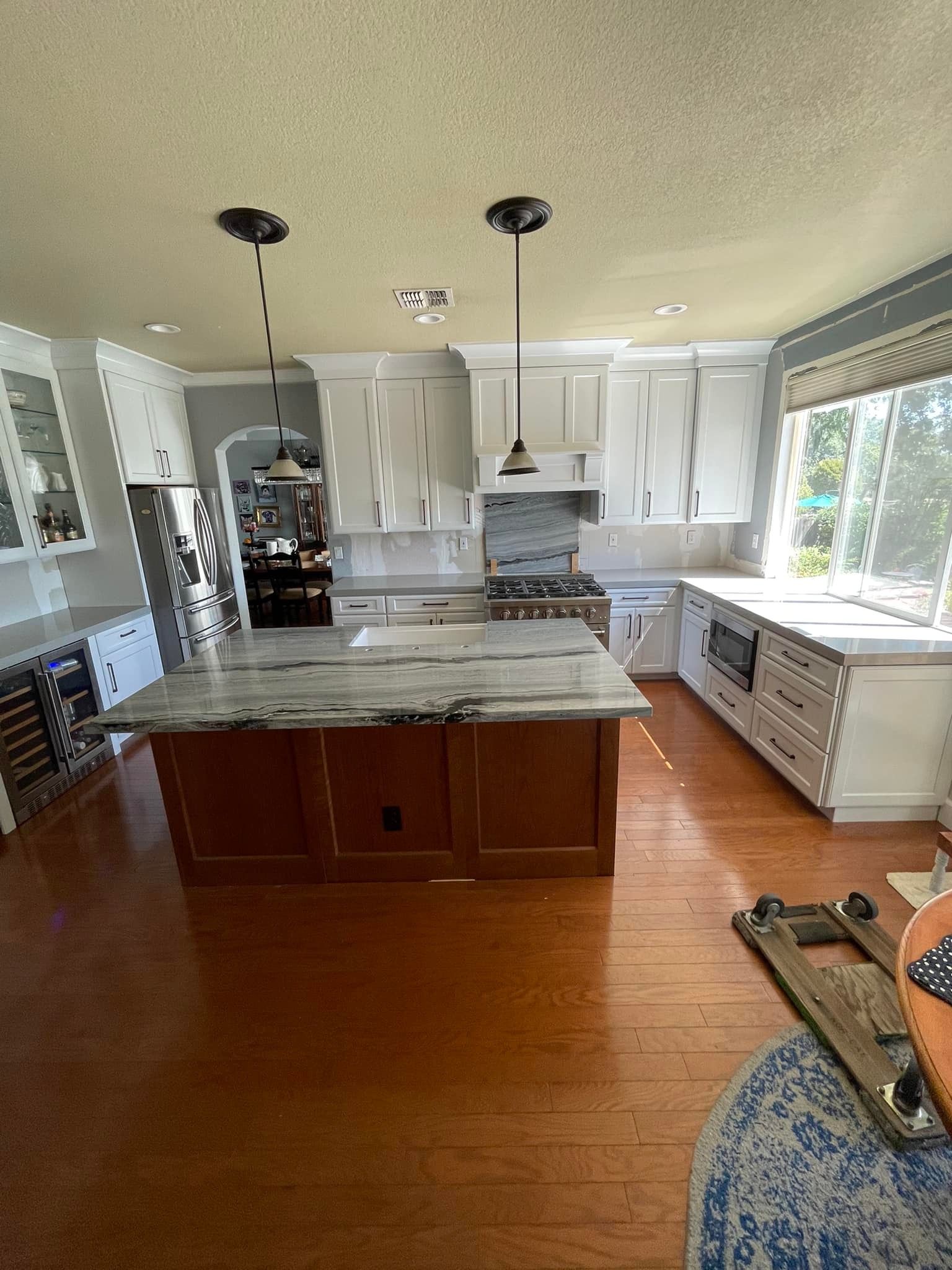 Spacious kitchen with a dark wood island and white cabinets. Wooden floors and large windows provide natural light.