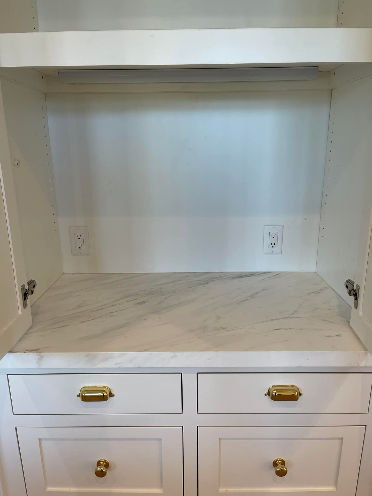 White built-in cabinet with drawers, marble-look countertop, and an upper recessed area with outlets.