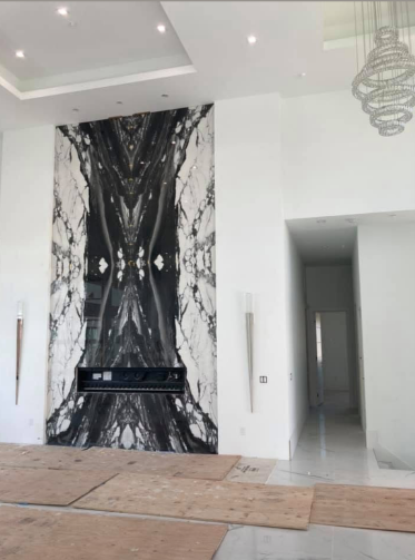 Dramatic black and white marble fireplace in a modern home, with tall ceilings and a hallway.