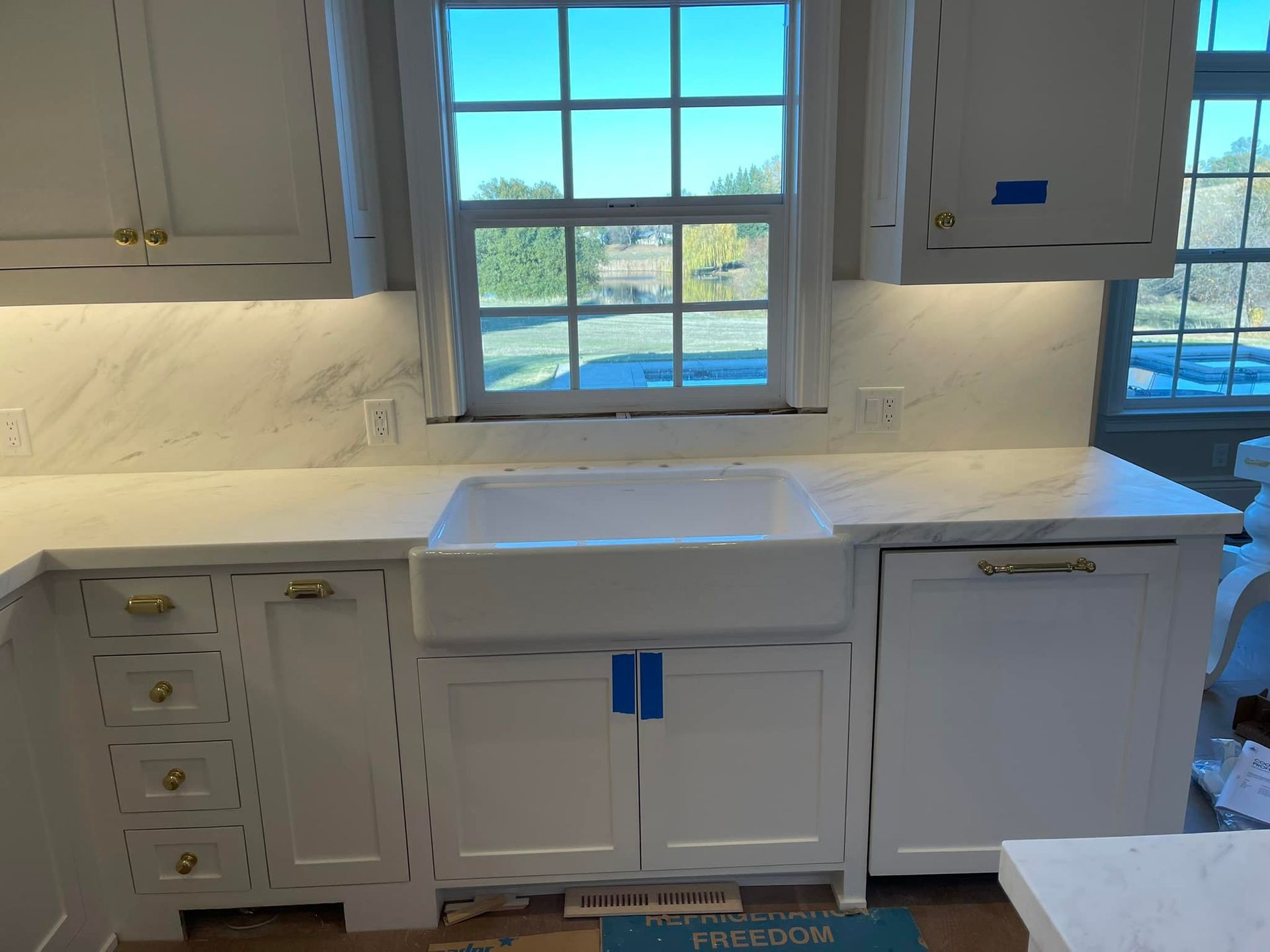 White kitchen with marble countertops, a farmhouse sink, and a window overlooking trees.