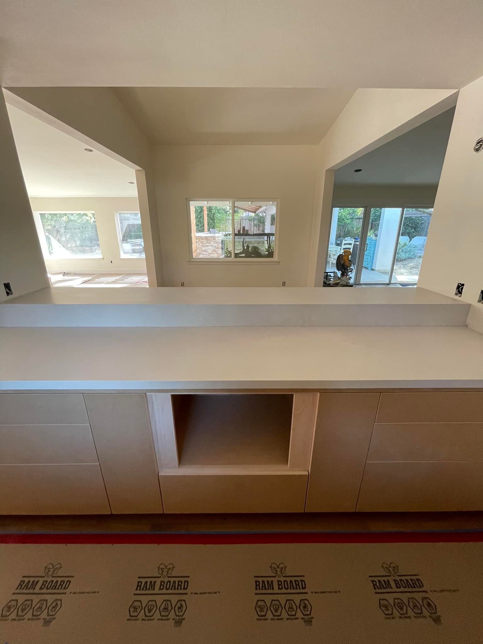 Kitchen countertop with cabinets and an open niche. Light wood cabinetry and a white countertop, with rooms visible beyond.
