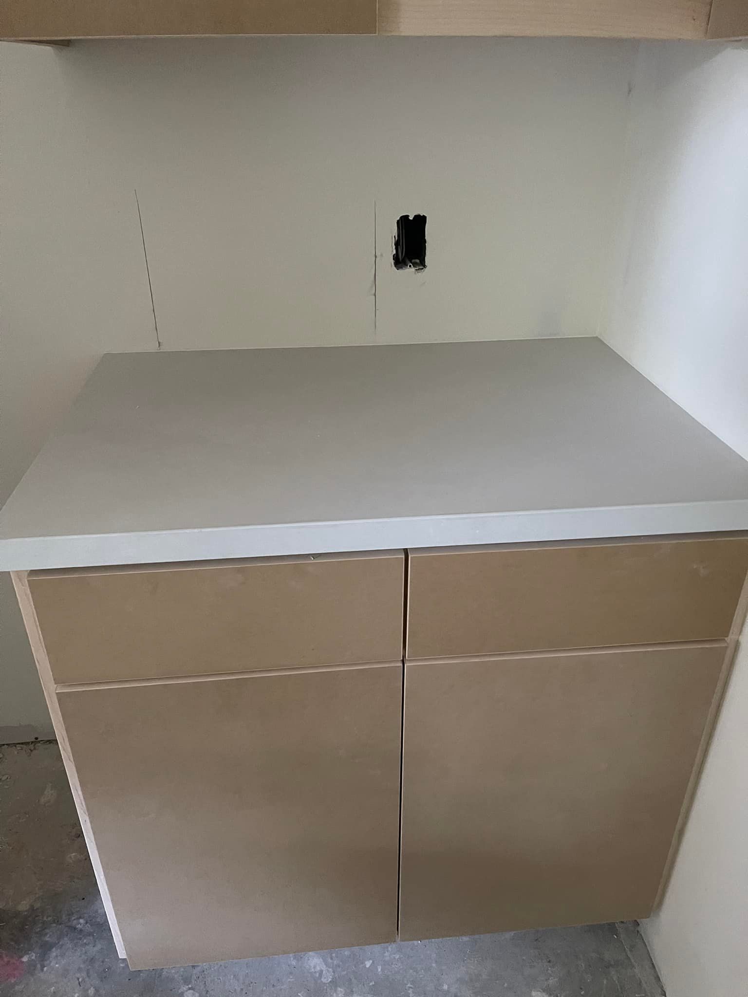 A light gray countertop sits on a two-door, light-wood-colored cabinet, with a blank wall behind.