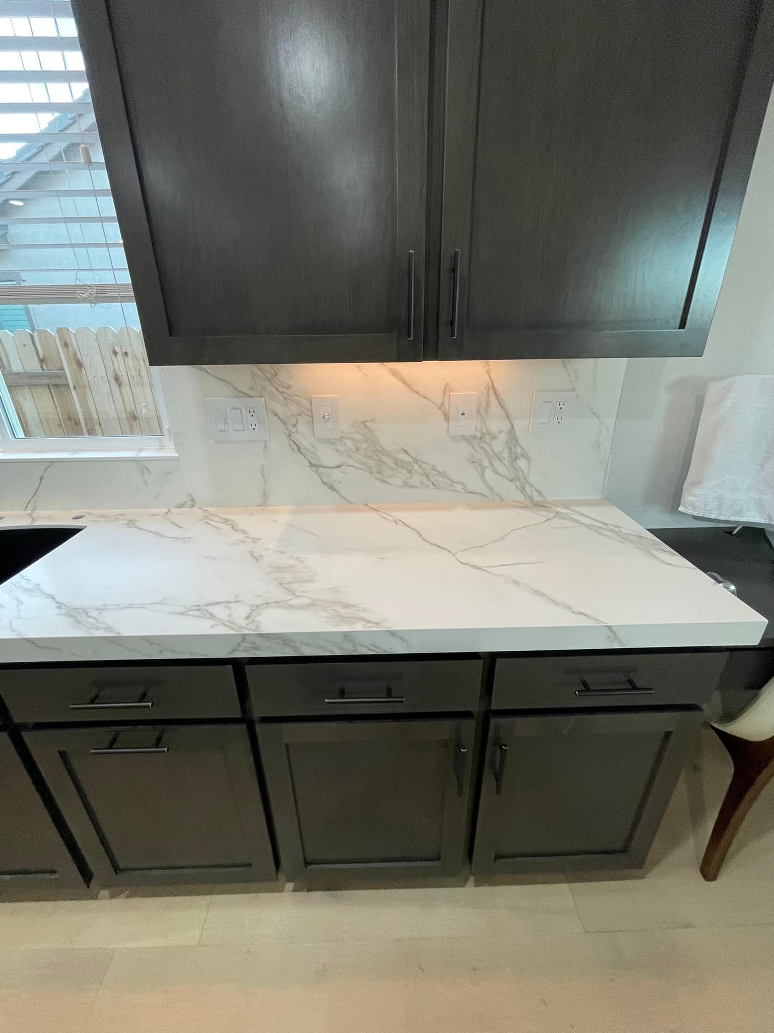 Kitchen cabinets with marble countertops. Dark cabinets, white and gray marble backsplash, and wood floor.