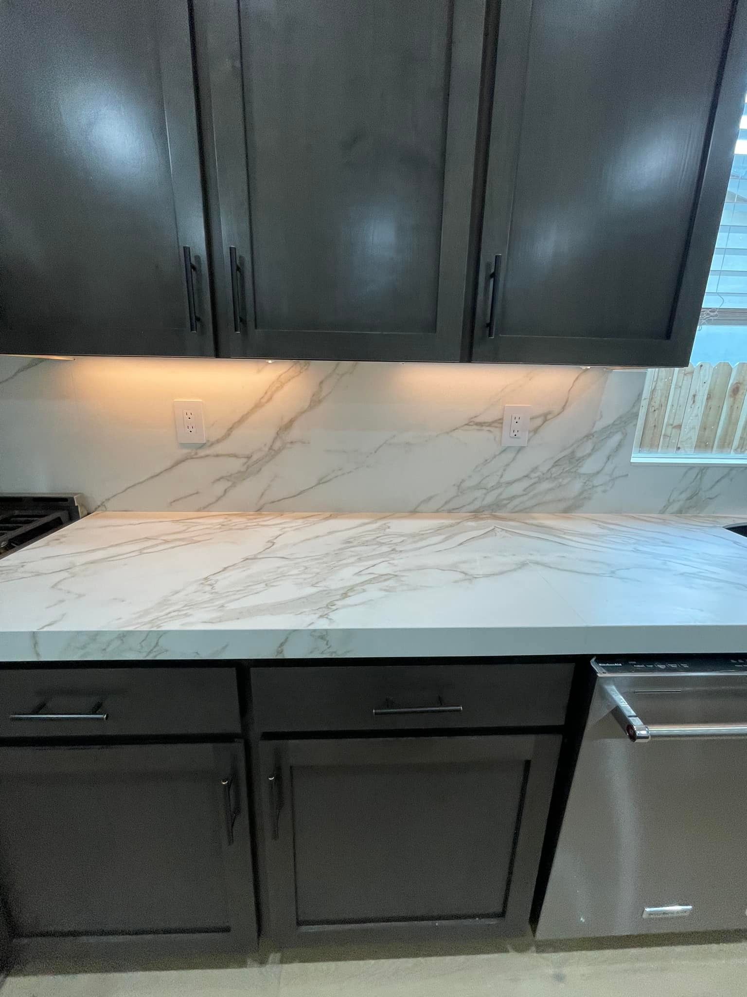 Dark gray kitchen cabinets with white marble countertops and backsplash.