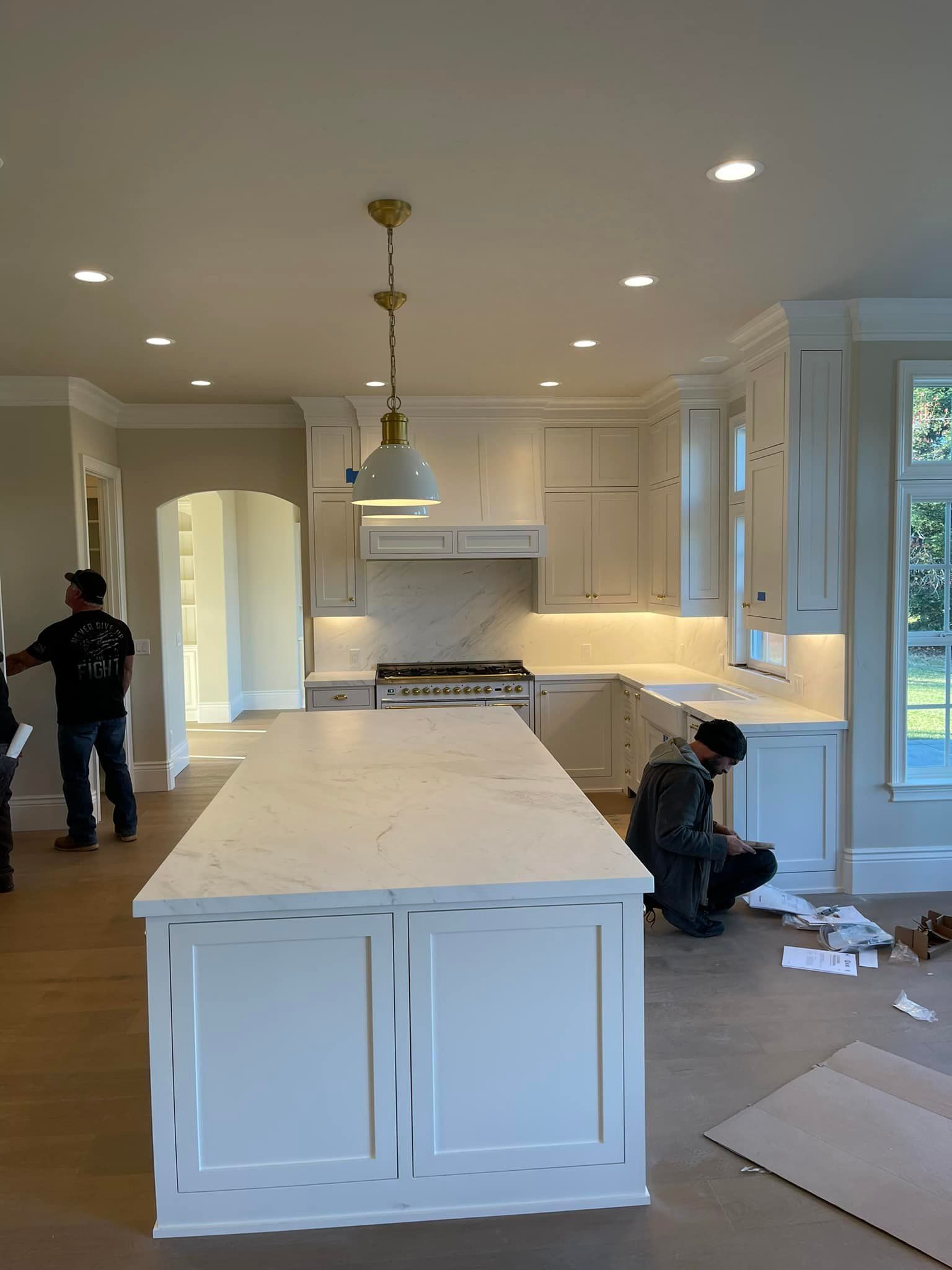 Kitchen under construction with white cabinets, island, and workers.