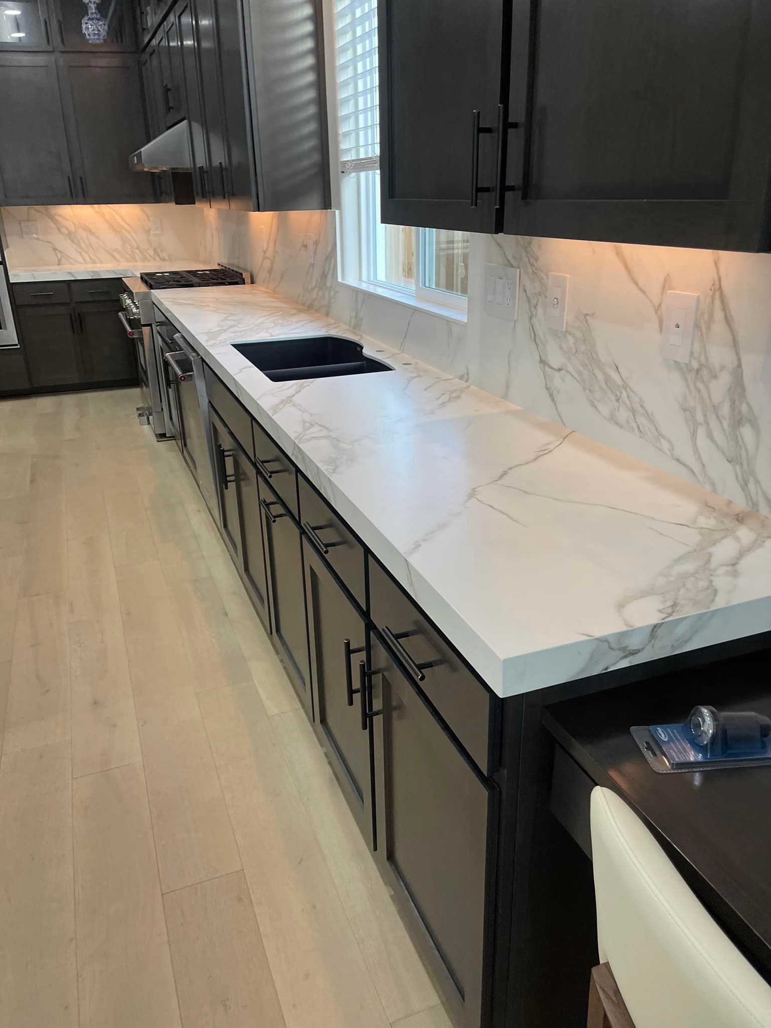 Modern kitchen with white marble countertops, dark cabinets, and a built-in cooktop.