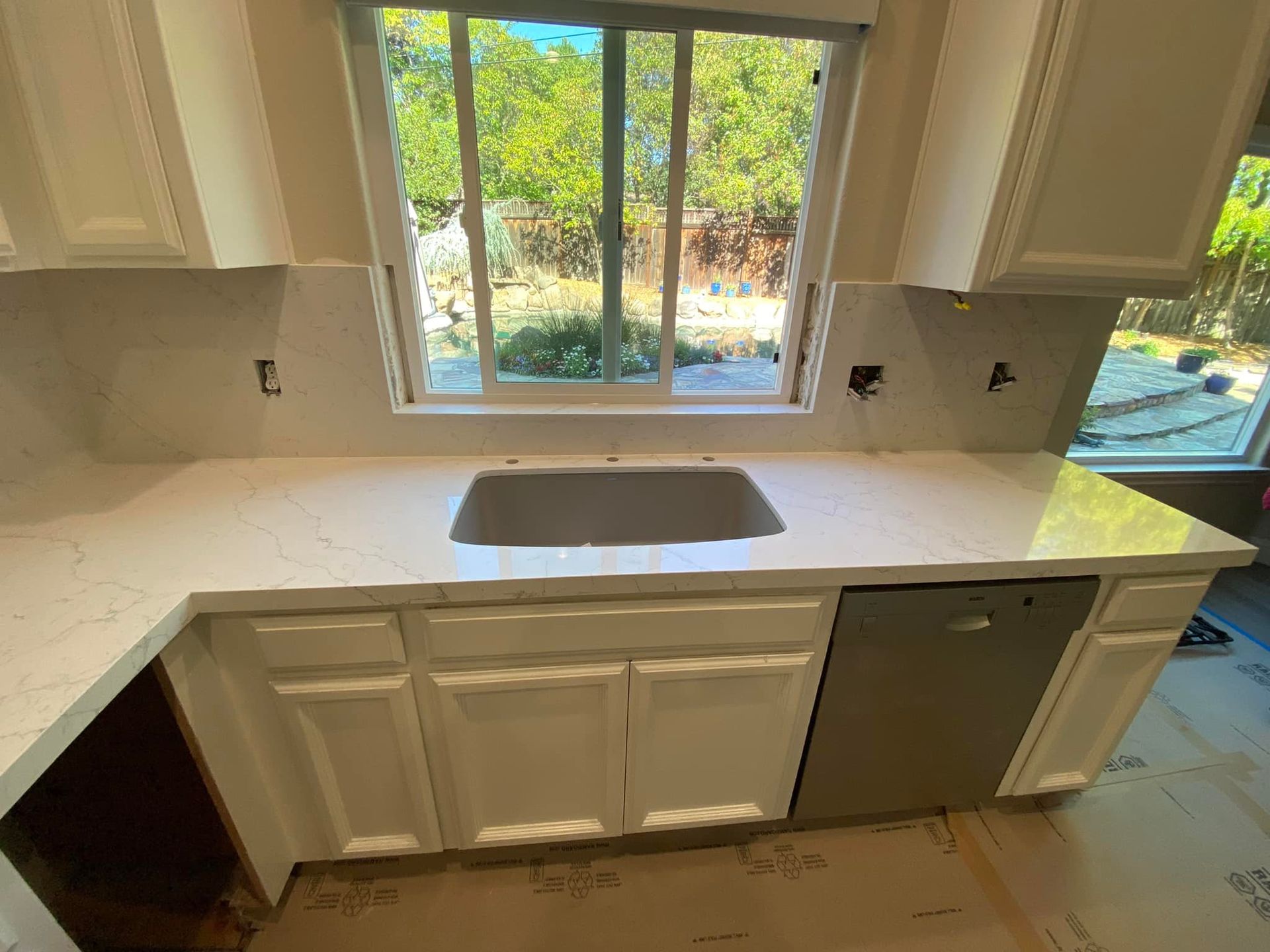 Kitchen with white cabinets, countertop, sink, and window overlooking a yard.