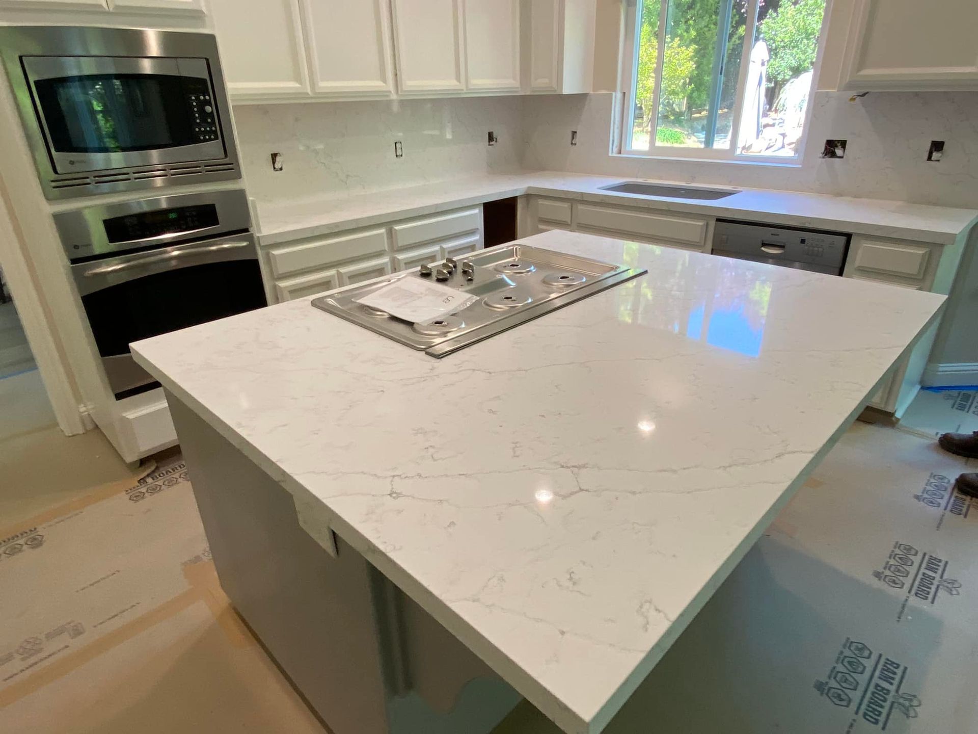 Modern kitchen with white countertops, island with cooktop, and stainless steel appliances.