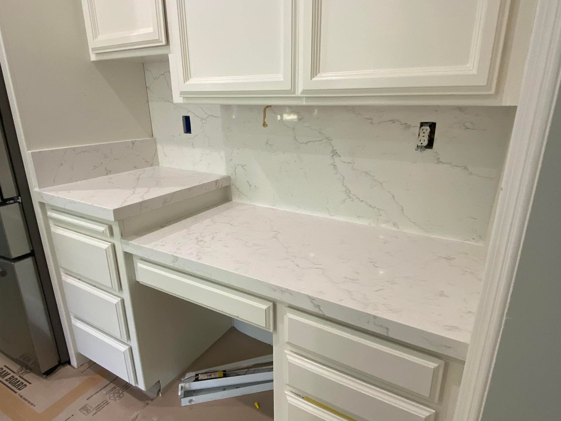 Built-in white desk with drawers and cabinets, white quartz countertop and backsplash.
