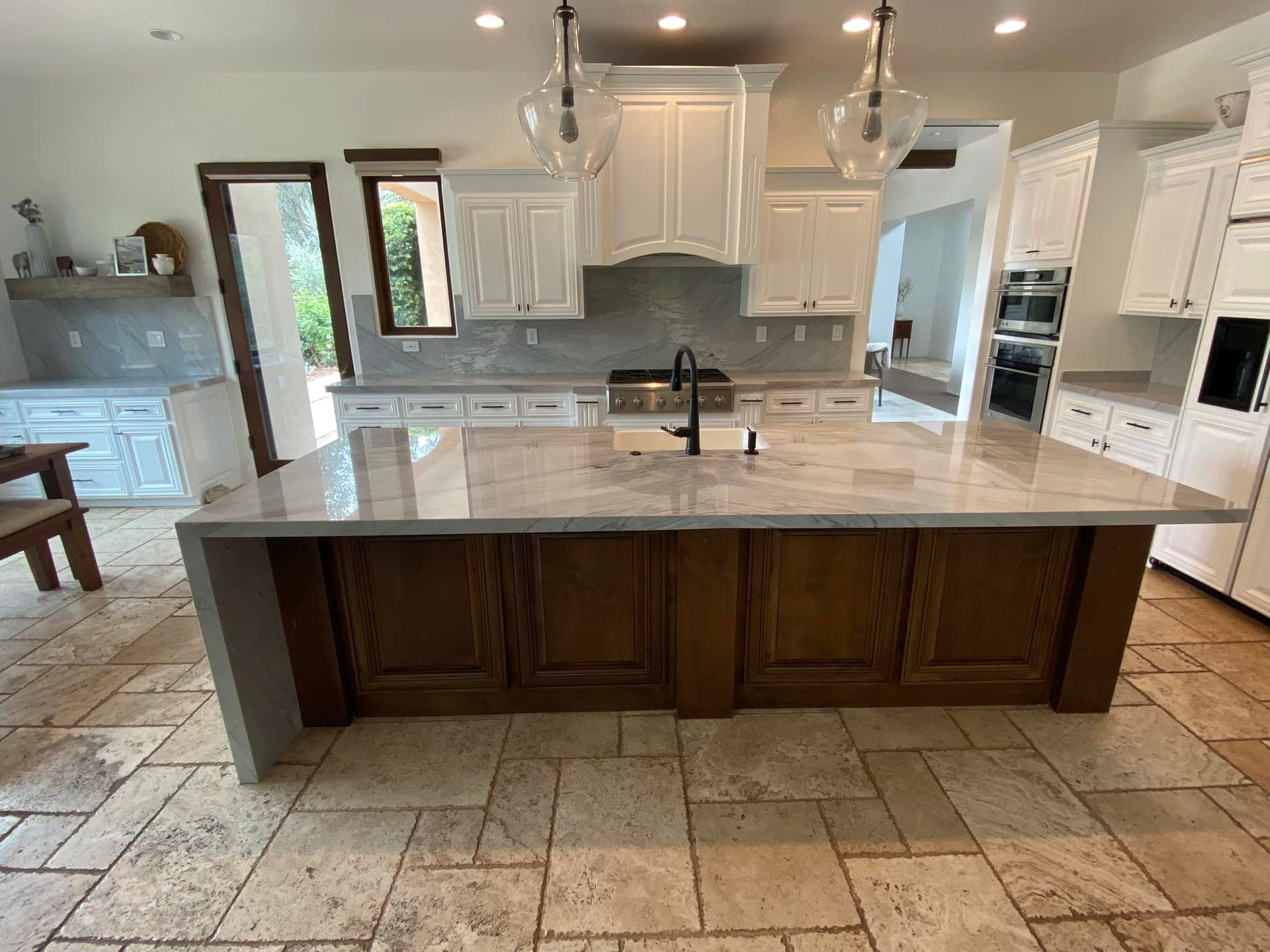 Spacious kitchen with large island, white cabinets, wood island base, granite countertops, and travertine floors.