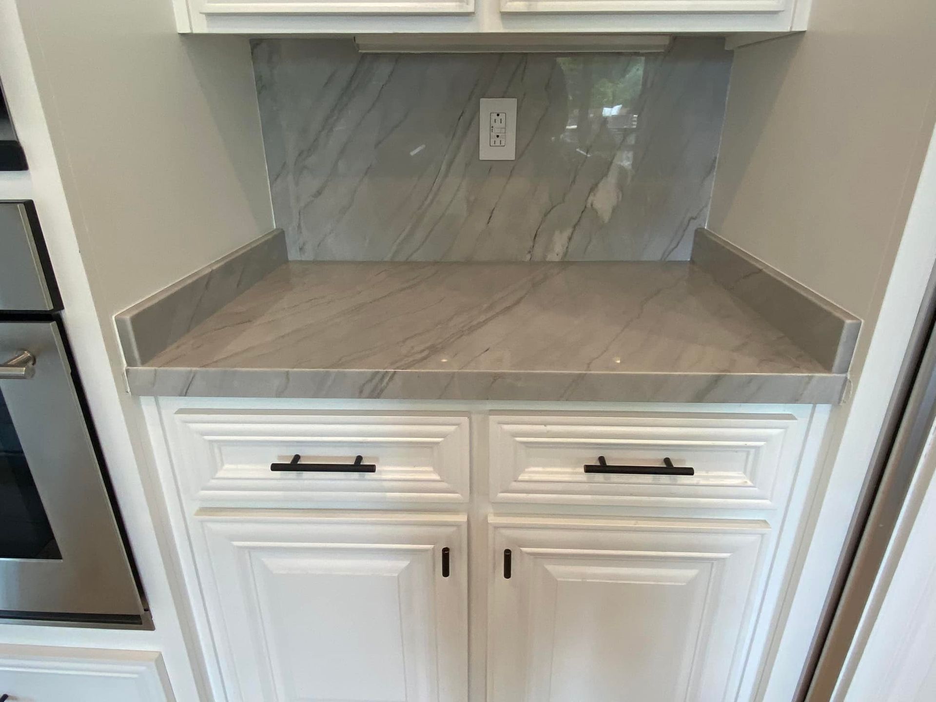 White cabinets with gray countertop and backsplash, black handles.