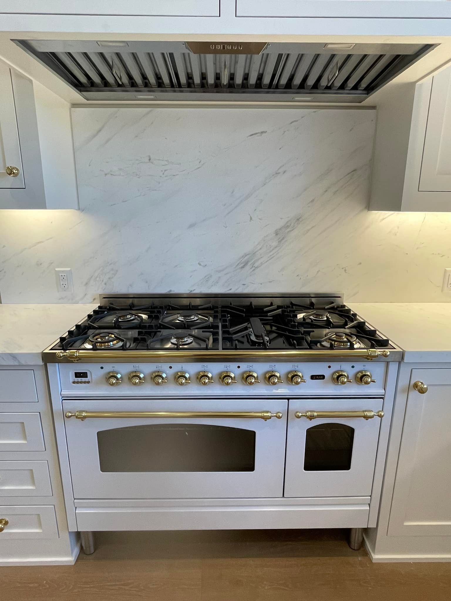 White kitchen with a large range, marble backsplash, and stainless steel range hood.
