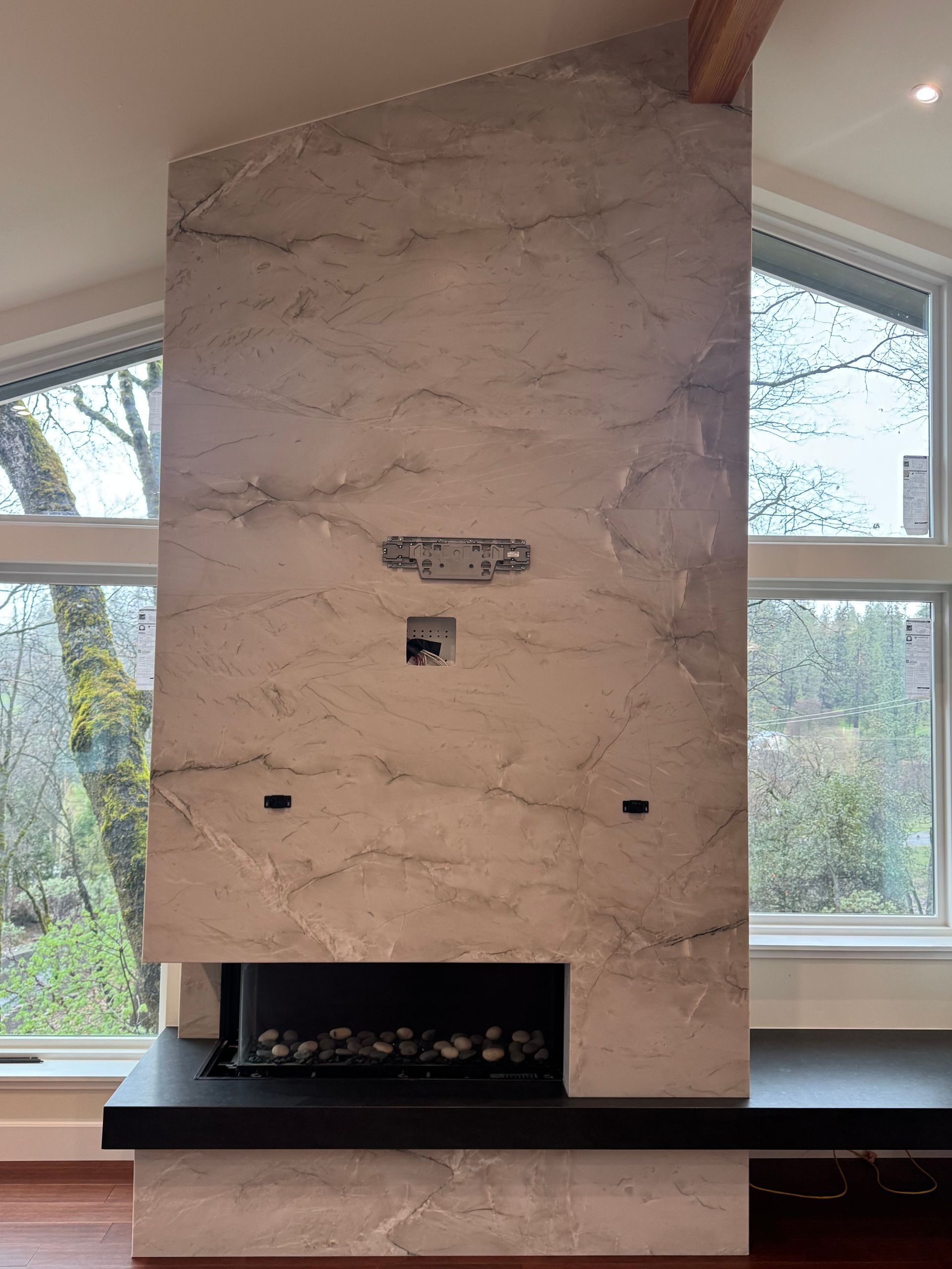 Modern fireplace with stone facade; windows flank the sides.