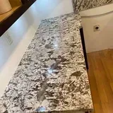 Granite countertop with light and dark gray swirls, next to a wooden floor and a wall.