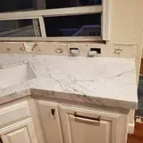 White marble countertop with white cabinets below, and a window above.