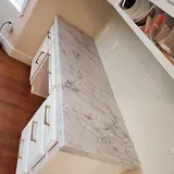 White marble countertop on white cabinets with gold handles.